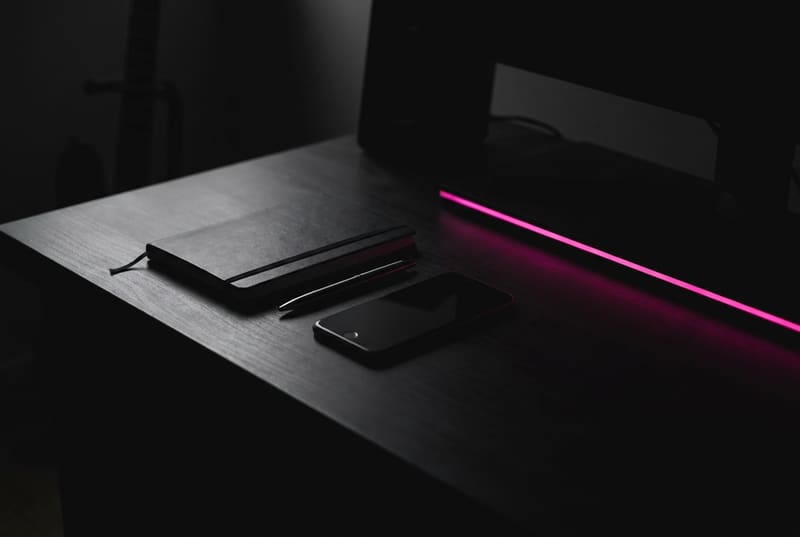 Escritorio oscuro con una libreta y un celular iluminados por una luz rosa, listos para planificar